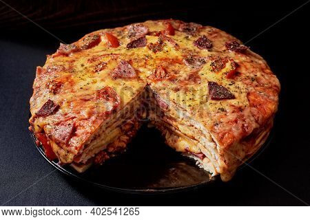 Italian Pizza Cake With Four Layers Full Of Grilled Salami, Ham And Moose Sausage. Black Background.