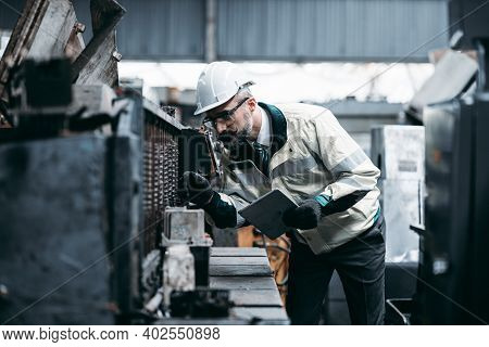 Technicians Man Or Engineer Holding Tablet For Checking Work In A Heavy Industrial Factory Behind. T