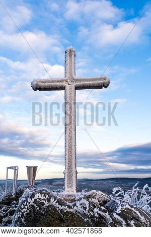Summit Cross Heavily Freezed With Snow And Ice At Cloudy Blue Sky