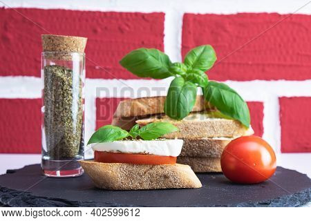 Basil, White Bread Croutons With Mozzarella, Spices And Tomato On A Stone Stand On A Brick Backgroun