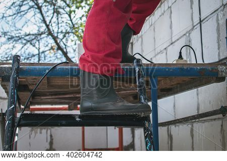 A Man The Builder Goes Down The Scaffolding. In The Frame There Are Legs In Boots. Concept Danger Du
