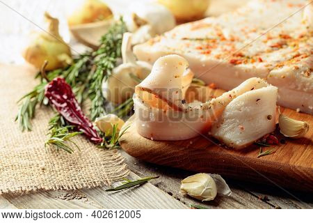 Slices Of Salted Spicy Lard On A Cutting Board. Lard With Spices And Herbs On A Old Wooden Table.
