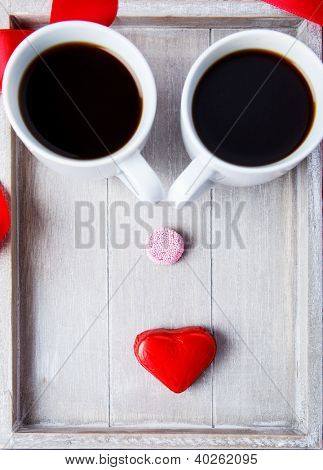 Due tazzine da caffè e dolci facendo la faccia buffa sul vassoio in legno