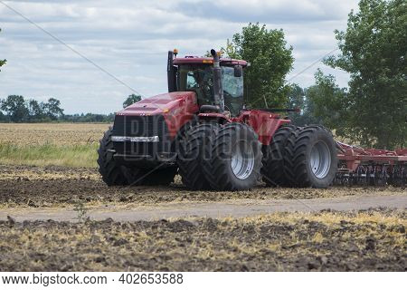 Red Tractor With A Plow On An Agricultural Field. August, Ukraine, Work In The Field With A Big Red 