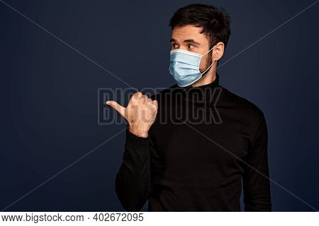 Young Man In Sterile Face Mask Pointing Index Finger Aside Isolated On Pacific Blue Background. Epid