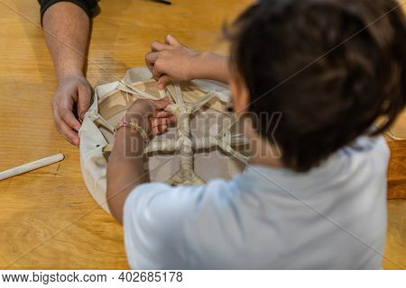 Rear View From Above Of A Child, A Young Boy, Learning To Knot The Loose Ends Of A Sin Together To C