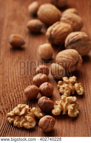 Walnuts and hazelnuts. Still life from whole nuts and kernels on brown textured wooden background. Selective focus on kernels. Healthy food. Vegetarian food