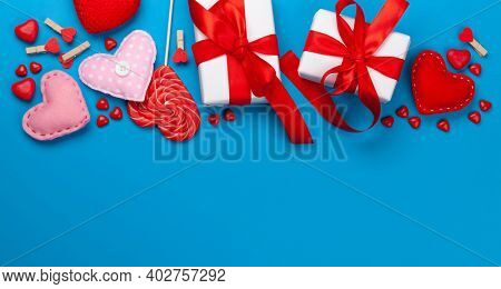 Valentines day greeting card template. Gift boxes, heart decor and candy sweets over blue background. Top view flat lay with copy space