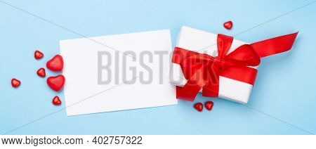 Valentines day greeting card template. Gift box and heart candy sweets over blue background. Top view flat lay with copy space