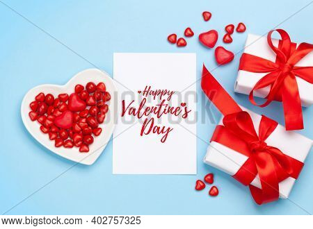 Valentines day greeting card. Gift boxes and heart candy sweets over blue background. Top view flat lay