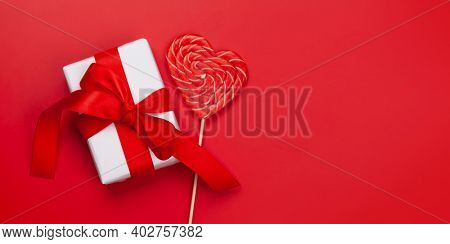 Valentines day greeting card template. Gift box and heart candy lollipop over red background. Top view flat lay with copy space