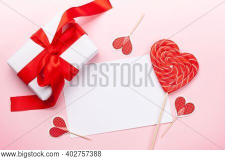 Valentines day greeting card. Gift box, heart decor and candy sweets over pink background. Top view flat lay with copy space