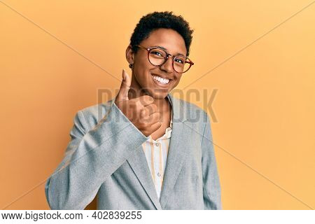 Young african american girl wearing business jacket and glasses doing happy thumbs up gesture with hand. approving expression looking at the camera showing success. 
