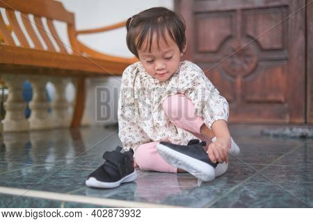 Cute Little Asian 2 Year Old Toddler Girl Sitting And Concentrate On Putting On Her Black Shoes, Sne