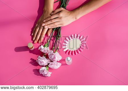 Top View Of Female Hands Near Palette Of False Nails, Carnation Flowers, And Bottles Of Cuticle Remo