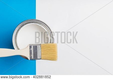 An Open Can Of White Paint And A Brush On A Blue And White Background. Execution Of Painting Works.
