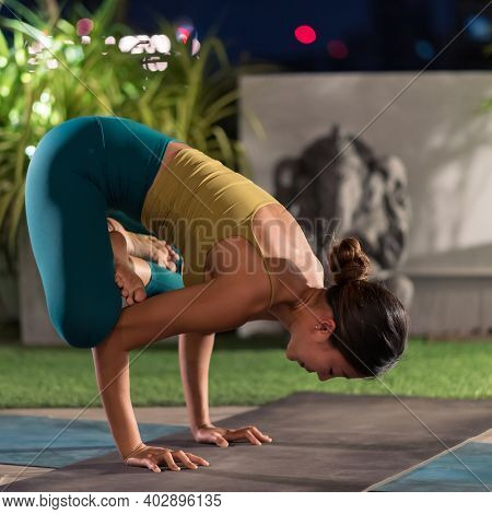 Asian female woman in sportswear bra pants practicing yoga during city lockdown alone in her apratment with background of cityscape illumination at night. Work out fitness healthy lifestyle concept.