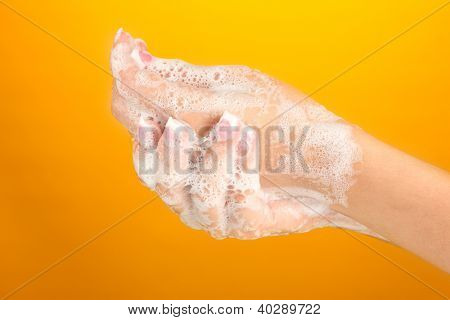 มือของผู้หญิงใน soapsuds บนพื้นหลังสีส้มอย่างใกล้ชิด