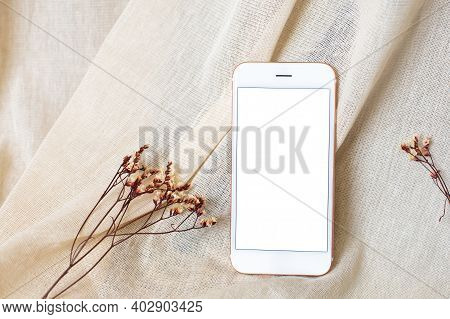 Mobile Phone And Dry Flowers On Beige Natural Cotton Fabric Background. Styled Stock Mock Up