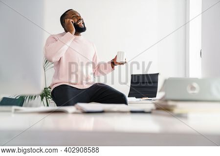 Afro american smiling businessman talking on mobile phone while sitting at the office desk