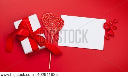Valentines day greeting card template. Gift boxes and heart candy sweets over red background. Top view flat lay with copy space