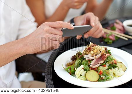 technology and people and concept - close up of couple with smatphone taking picture of food at restaurant terrace