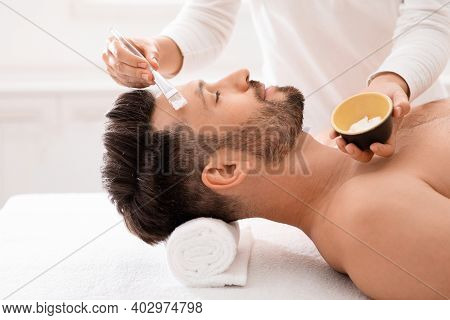 Middle-aged Handsome Man Having Face Treatment At Male Spa. Cosmetologist Applying White Clay Mask O