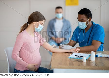 African American Doctor Giving Covid-19 Vaccine Injection To Young Pregnant Woman At Health Centre. 