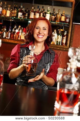 Beautiful redhead barmaid with bottle behind bar counter 