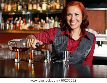 Beautiful redhead barmaid making shots