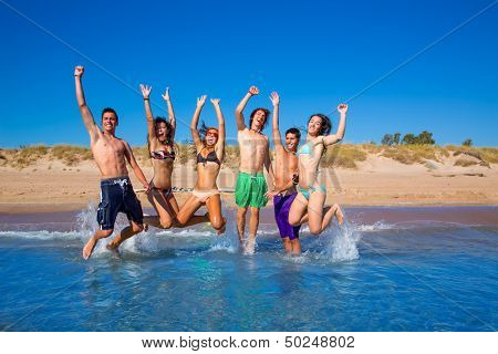 Happy excited teen boys and girls group jumping at the beach splashing water