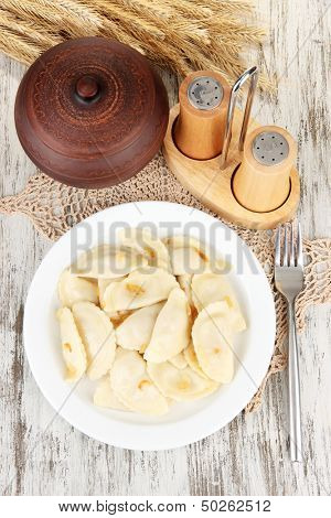 Tasty dumplings with fried onion on white plate, on wooden background
