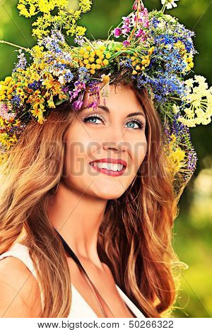 Portrait of a romantic smiling young woman in a circlet of flowers outdoors.