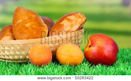 Empanadas al horno frescas con frutas, en cesta de mimbre, sobre hierba, sobre fondo brillante