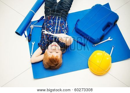 Funny little mechanic boy with wrench tools lying on a blueprint 