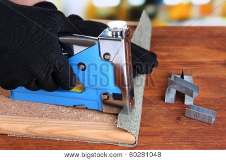 Fastening fabric and board using construction stapler on bright background
