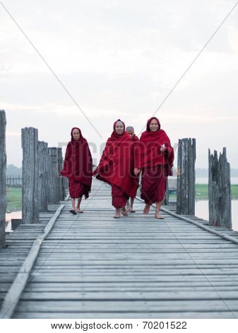 MANDALAY, MYANMAR - JAN 19, 2014: Unidentified monks from local Buddhist temple in Amarapura crossing U Bein bridge at early morning. The bridge is famous historical and cultural heritage of country 