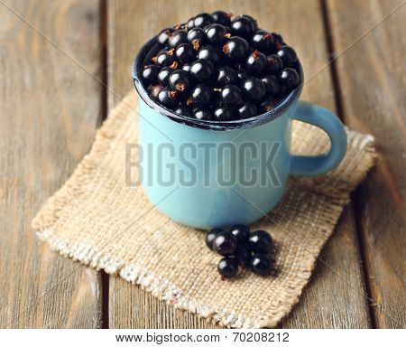 Ripe blackcurrants in mug on sackcloth napkin, on wooden background.