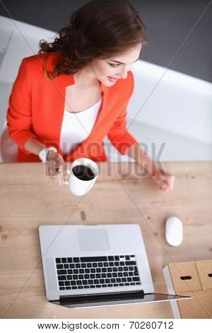 Attractive woman sitting at desk in office, working with laptop