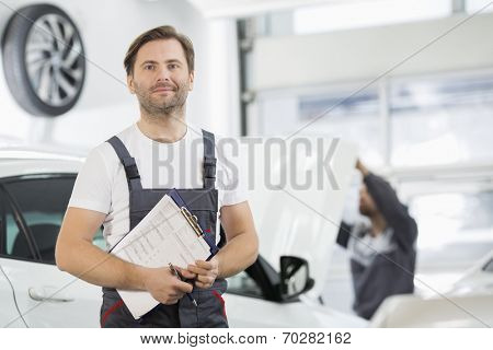 Portrait of confident male maintenance engineer with clipboard in car repair shop