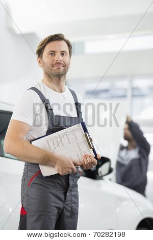 Portrait of confident male automobile mechanic with clipboard in car repair store