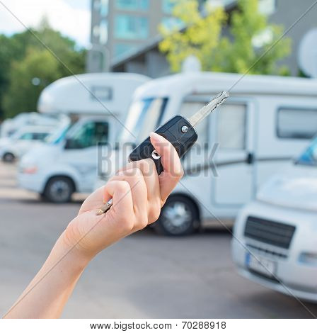 Woman's Hand With Key Against Campervans Background.