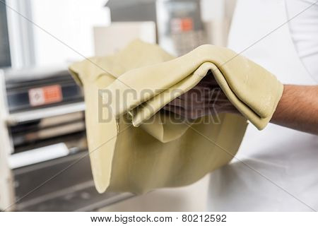 Midsection of male chef holding spaghetti pasta sheet at commercial kitchen