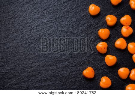 Orange heart shaped pills or candy on grunge black slate background. Copy space.