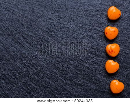 Orange heart shaped pills or candy on grunge black slate background. Copy space.