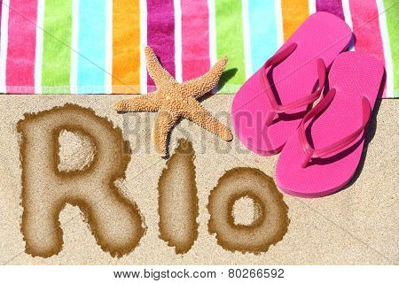 Rio. Overhead view ot the word RIO written on beach sand with a colorful striped towel, pink thongs and a starfish conceptual of a summer vacation and travel in Rio de Janiero, Brazil