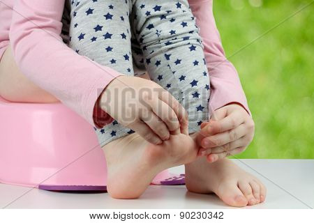 Children's Legs Hanging Down From A Chamber-pot On A Green Background