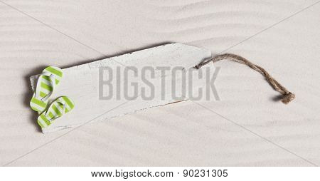 Summer background with a wooden sign and bathing shoes in the sand.