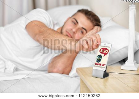 Beautiful young man waking up with mobile alarm clock