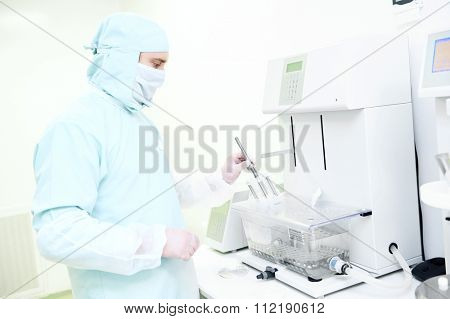 Pharmaceutical scientific male researcher in protective uniform working with disintegration tester at pharmacy industry manufacture factory laboratory. Worker holding basket rack assembly in his hand.